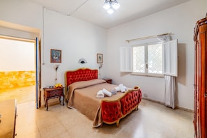 A room with a red tufted bed, a small bedside table, a window with curtains, and a door leading to another room. - Villino Salentum With Private Pool and Garden (Racale)