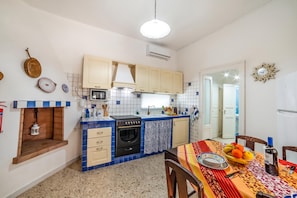 A compact kitchen with a stove, oven, and sink, a dining area with a table set for two, and a small window. - Villino Salentum With Private Pool and Garden (Racale)