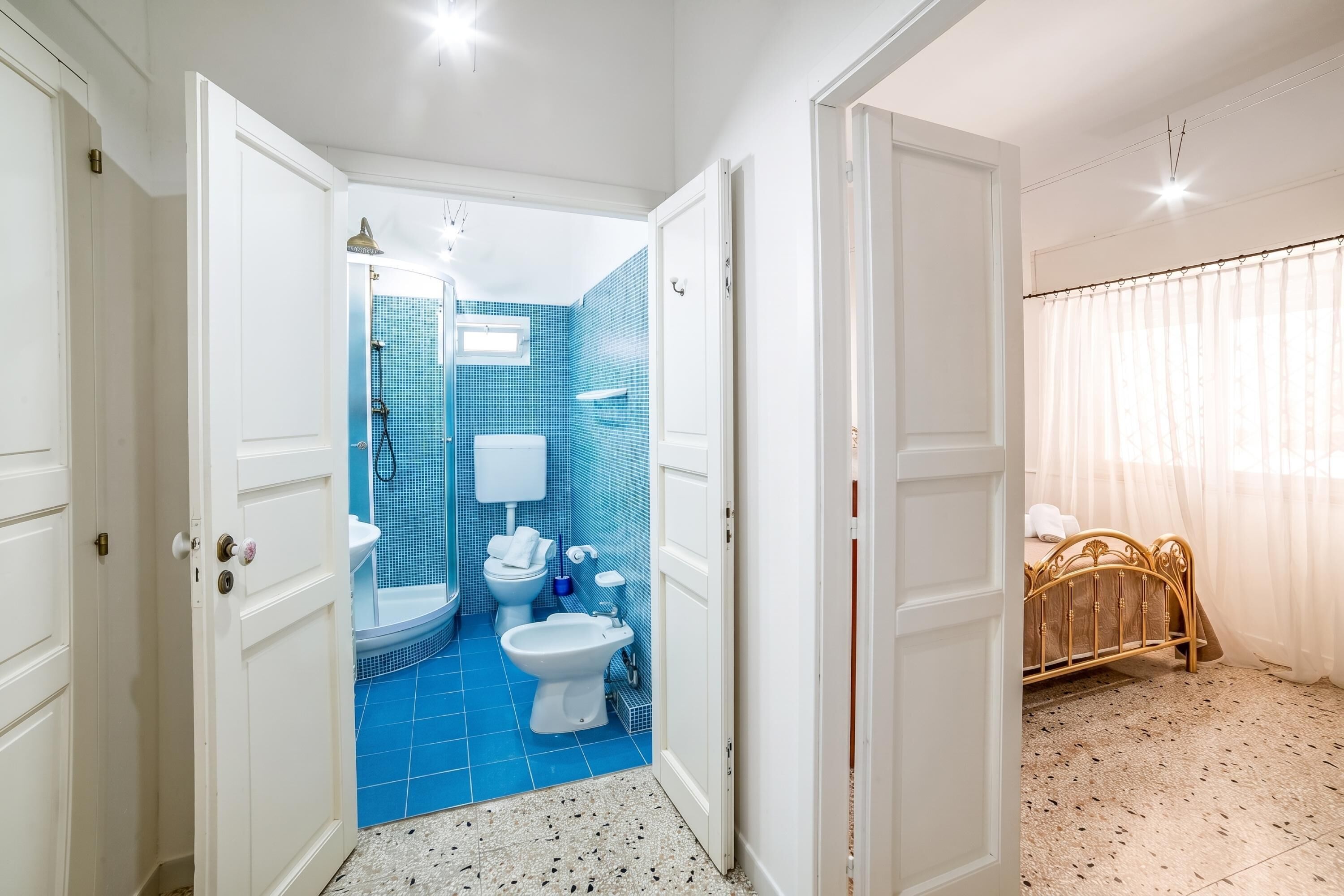 A bathroom with a blue tiled wall, a white toilet, a sink, and a shower.