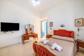 Habitació d'hotel amb un llit, una televisió, un mirall, una petarrera i una porta que dona a una altra habitació.
