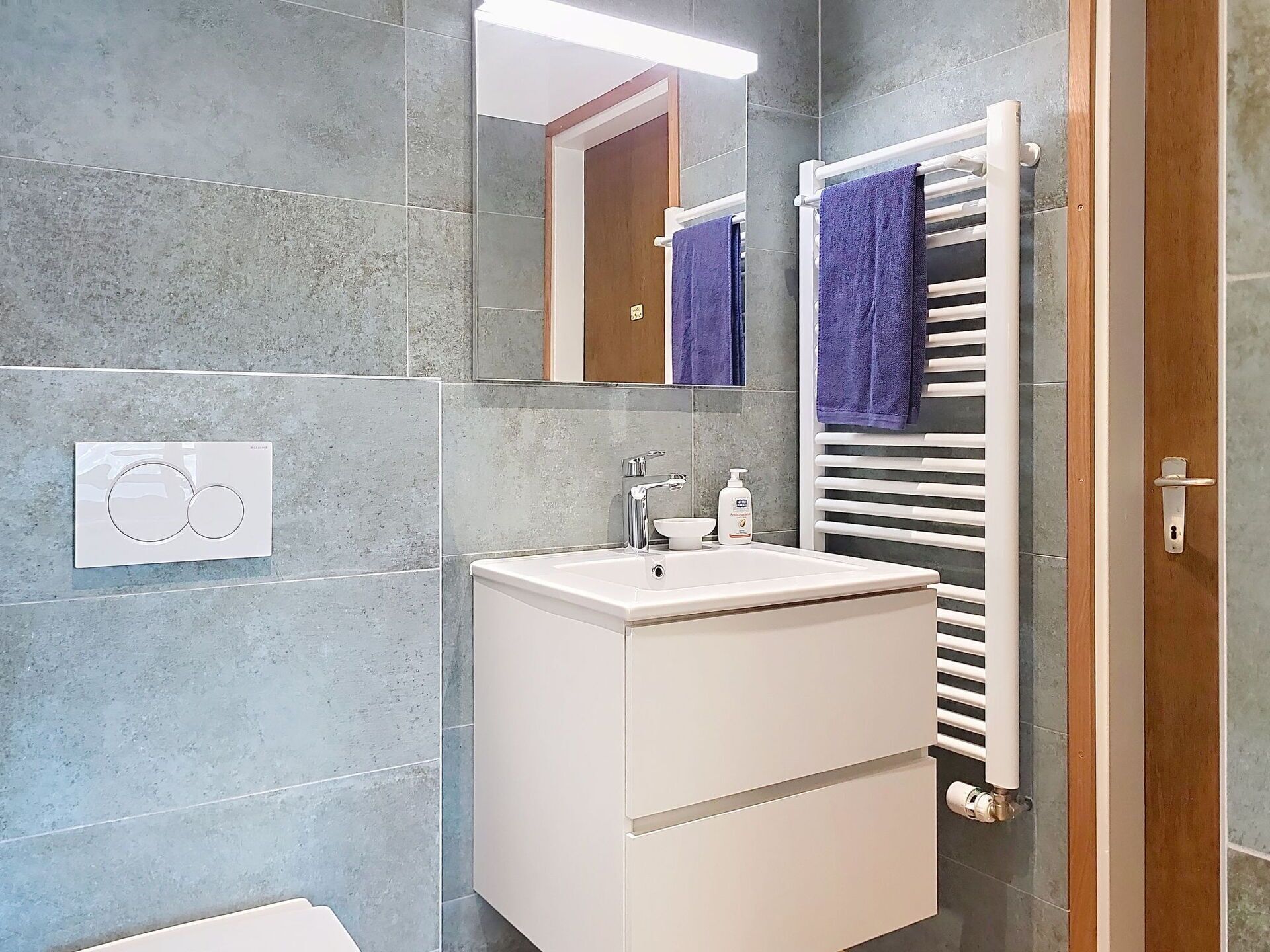 A modern bathroom with a white sink, mirror, and towel rack.