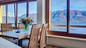 Ein Essbereich mit Tisch, Stühlen und einer Blumenvase. Große Fenster bieten Blick auf Berge und einen See.