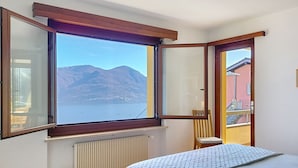 Ein Schlafzimmer mit einem großen Erkerfenster mit Blick auf einen See und Berge.