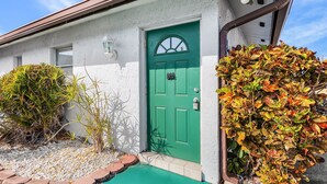 Una casa con puerta verde, un pequeño porche y un jardín con hojas otoñales.