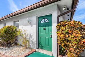 Ein Haus mit grüner Tür, einer kleinen Veranda und einem Garten mit Herbstlaub.