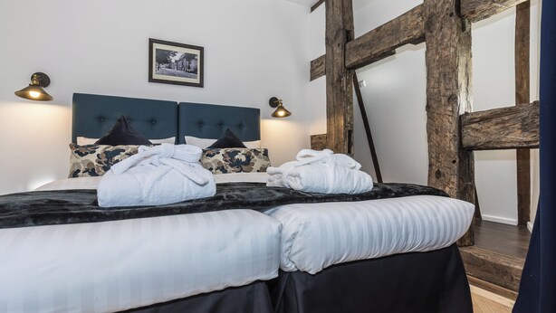 Un dormitorio con una cama grande, dos lámparas de noche, un cuadro enmarcado en la pared y vigas de madera a la vista.