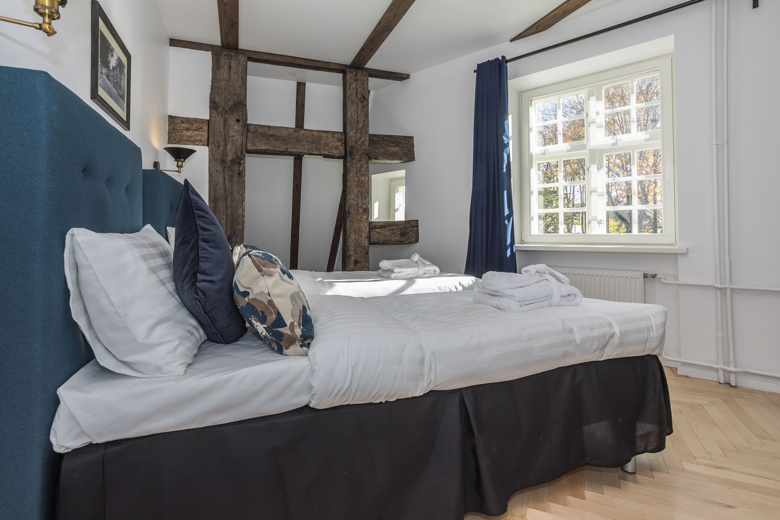 Une chambre à coucher avec un lit, une structure en poutres apparentes, une fenêtre avec vue et un radiateur.