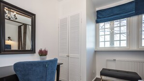 Una habitación con una silla azul, un armario blanco, un banco, una ventana con cortina azul y un radiador.