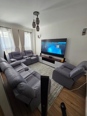 A modern living room with a flat-screen TV, grey sofas, a wooden floor, and a ceiling fan. - Lovely 1-bedroom apartment in tranquil Nairobi perfect for your stay (Nairobi)