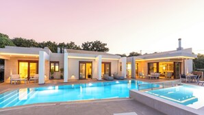 En moderne villa med swimmingpool, udendørs møbler og en velbelyst patio.