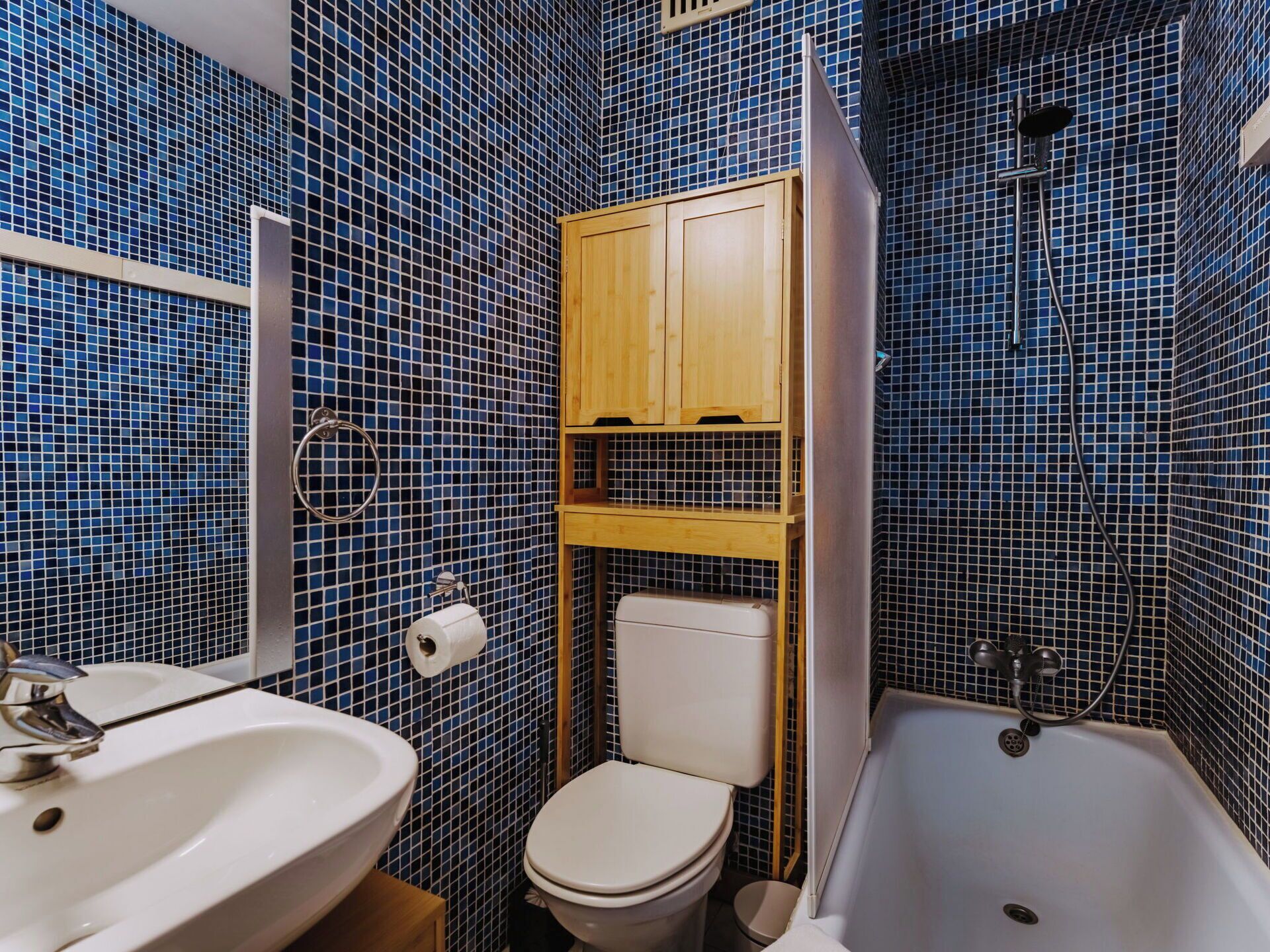 A bathroom with a white sink, toilet, and bathtub. The walls are covered with blue mosaic tiles.
