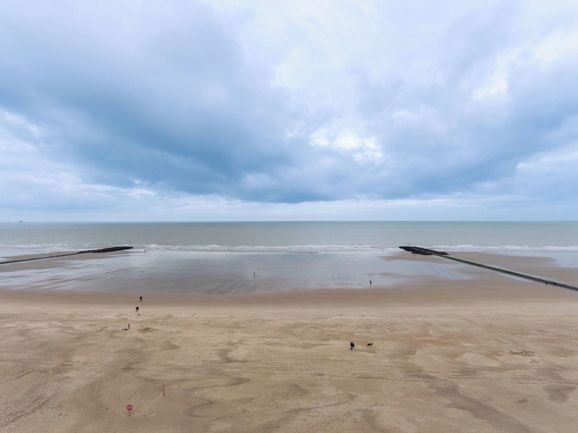 A wide sandy beach with a calm sea under a cloudy sky.