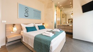 A modern hotel room with a large bed, bedside lamps, a bathroom mirror, and a mounted TV. - Titan Villas - Villa Kronos (Chania)