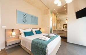 A modern hotel room with a large bed, bedside lamps, a bathroom mirror, and a mounted TV. - Titan Villas - Villa Kronos (Chania)