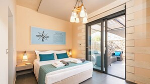 A bedroom with a bed, bedside tables, a wall-mounted artwork, and a sliding glass door leading to an outdoor seating area. - Titan Villas - Villa Kronos (Chania)