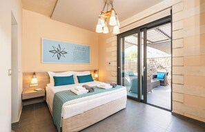 A bedroom with a bed, bedside tables, a wall-mounted artwork, and a sliding glass door leading to an outdoor seating area. - Titan Villas - Villa Kronos (Chania)
