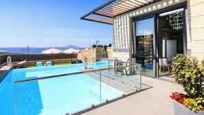 A modern outdoor pool area with a glass balustrade, stone walls, and a view of the sea. - Titan Villas - Villa Kronos (Chania)