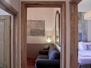 A room with a wooden door frame, a sofa, a bedside table, a lamp, a mirror, and a bed. - Donati Tower Loggia: in the heart of Florence with spectacular views of the Duomo (Firenze)