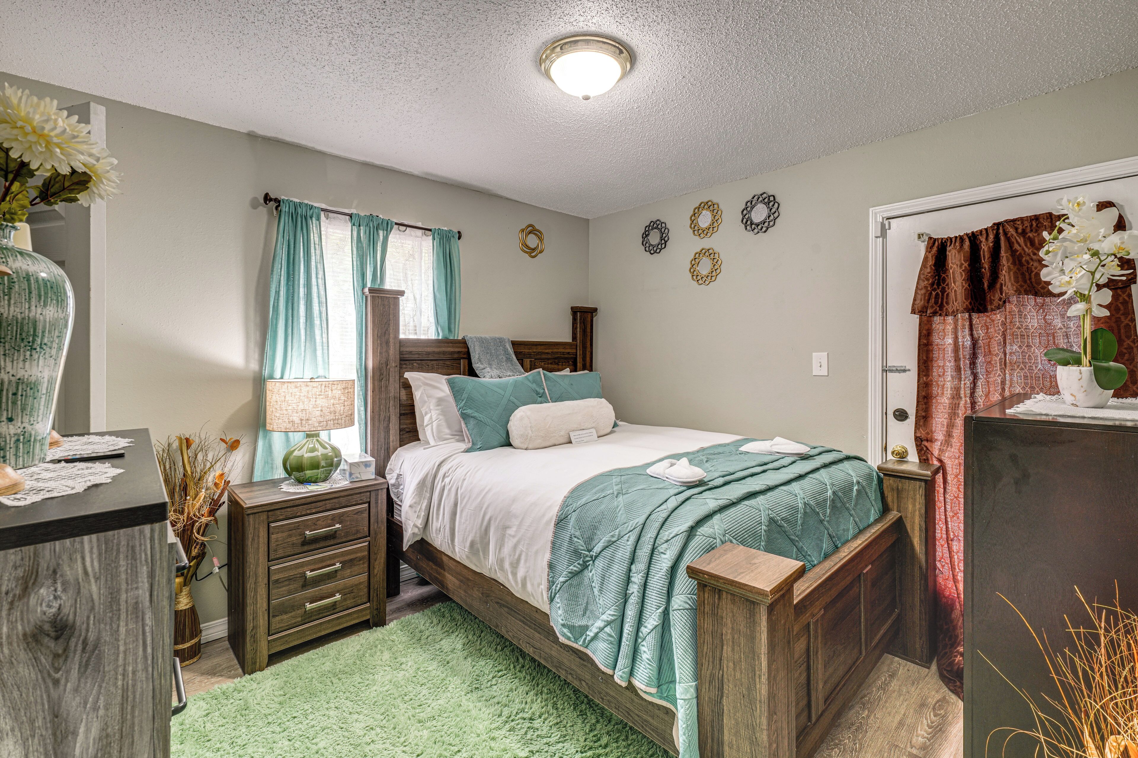 A bedroom with a bed, nightstand, dresser, and a green rug.