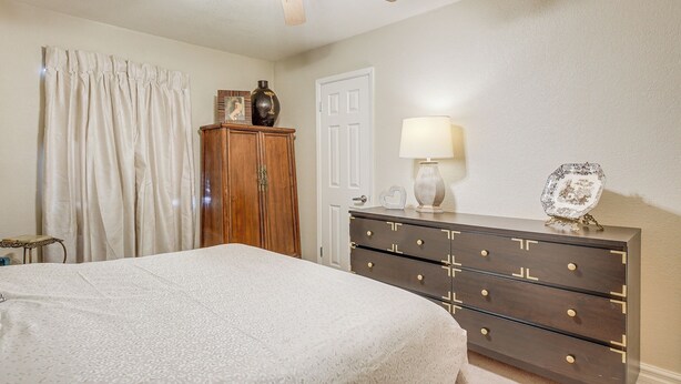 Une chambre à coucher comprenant un lit, une commode, un ventilateur de plafond, une lampe et une porte.
