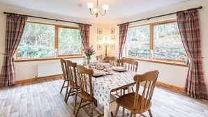 A dining room with a table set for six, wooden chairs, a chandelier, and large windows with curtains. - Stunning private villa for 8 people with WIFI, TV, terrace and panoramic view (Invermoriston)