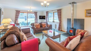 A cozy living room with leather sofas, a fireplace, a television, and a dining area with a table and chairs. - Stunning private villa for 8 people with WIFI, TV, terrace and panoramic view (Invermoriston)