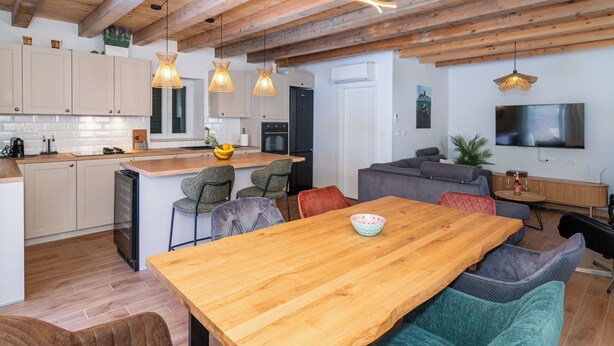 Eine moderne Küche mit Holzbalken, ein Essbereich mit Holztisch und ein Wohnbereich mit Sofa und Fernseher.
