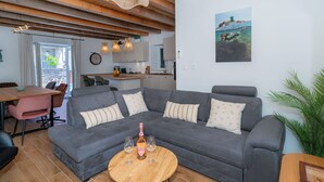 Ein modernes Wohnzimmer mit einem grauen Ecksofa, einem Holztisch und einem Essbereich mit einem rosa Stuhl.
