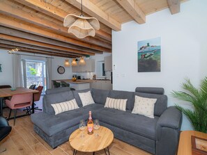 Ein modernes Wohnzimmer mit einem grauen Ecksofa, einem Holztisch und einem Essbereich mit einem rosa Stuhl.
