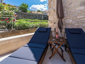 Eine Terrasse mit zwei Liegestühlen, einem Tisch mit Flasche und Gläsern sowie einer Steinsäule.