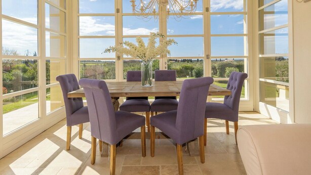 Ein Essbereich mit einem großen Tisch, sechs Stühlen, einer Chandelüster und Blick auf die Landschaft.