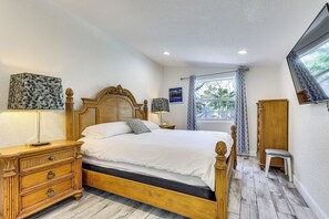 A bedroom with a wooden bed, a nightstand, a lamp, a window with curtains, and a wooden wardrobe. - 3 Mi to Las Olas Blvd: Tropical Getaway w/ Patio! (Fort Lauderdale)