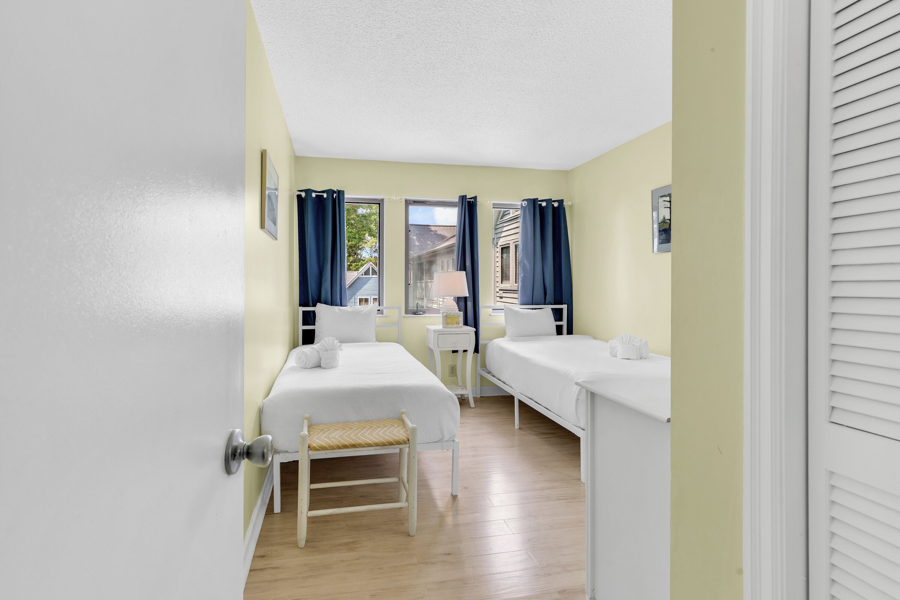 A room with two beds, a small table, a bench, and a window with curtains.