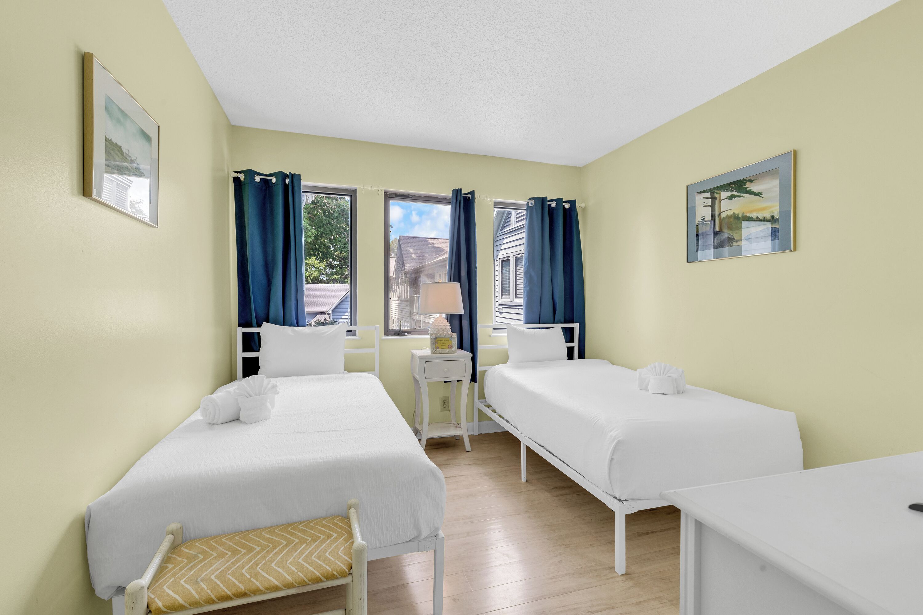 Ein Zimmer mit zwei Betten, einem Sessel, einem kleinen Tisch und einem Fenster mit Vorhängen.