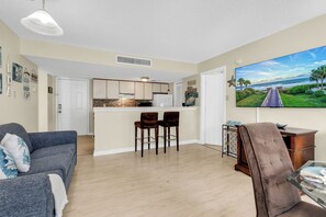A living room with a sofa, a chair, a TV, and a kitchen area with a bar. - Myrtle Beach Resort 6306 (Myrtle Beach)