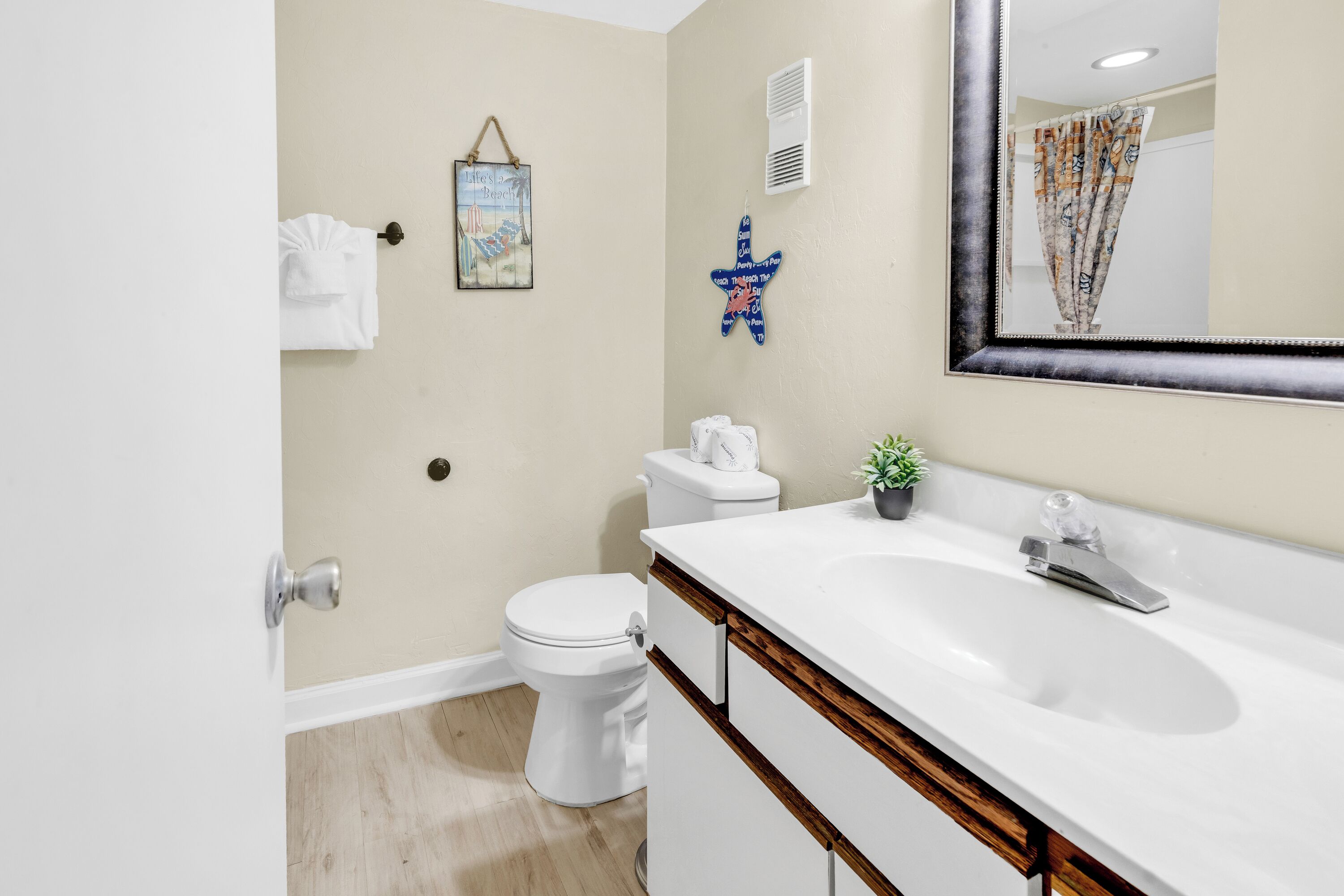 A bathroom with a white sink, a toilet, a mirror, and a wall-mounted air vent.