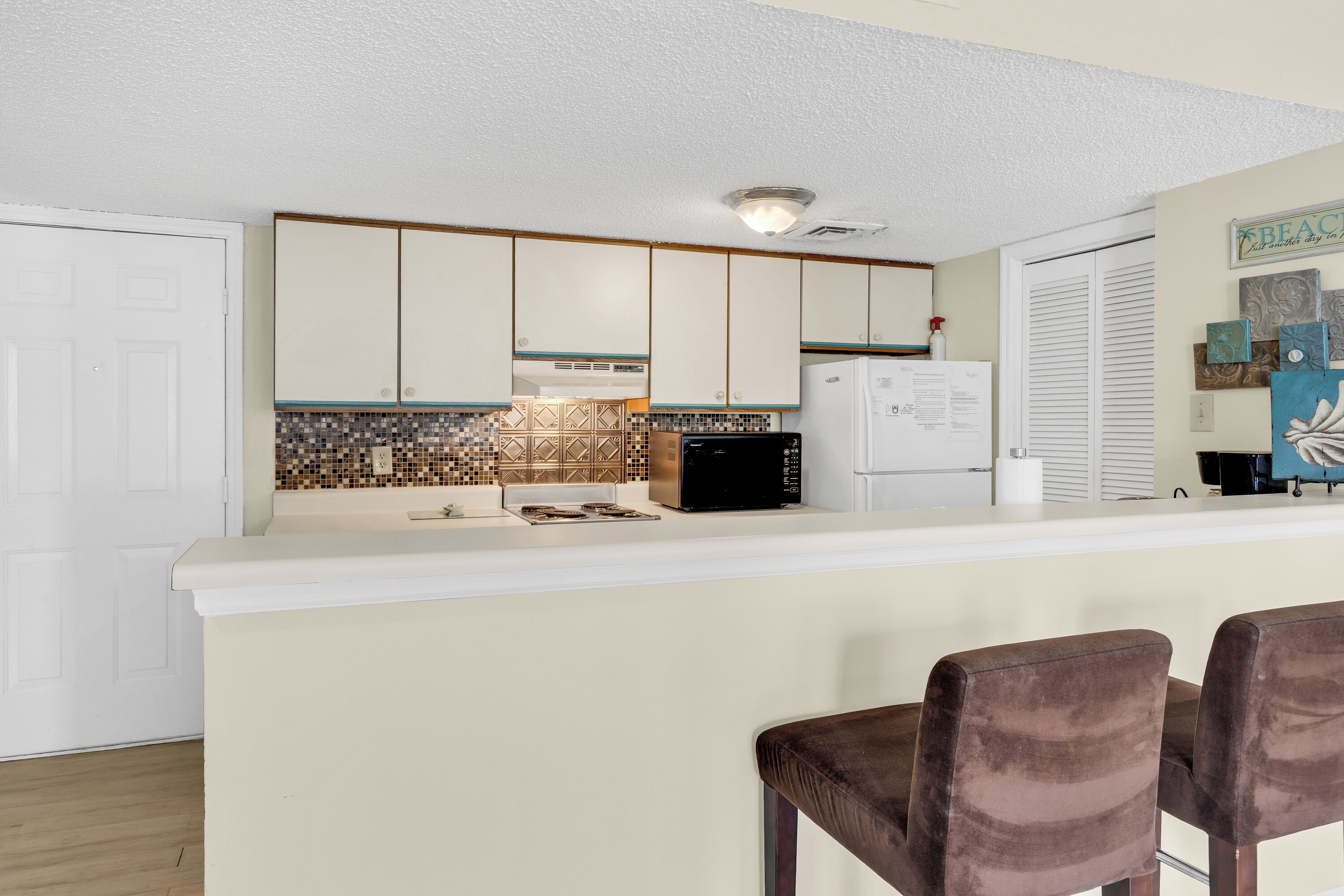 A kitchen with a white countertop, a black refrigerator, and a tiled backsplash.
