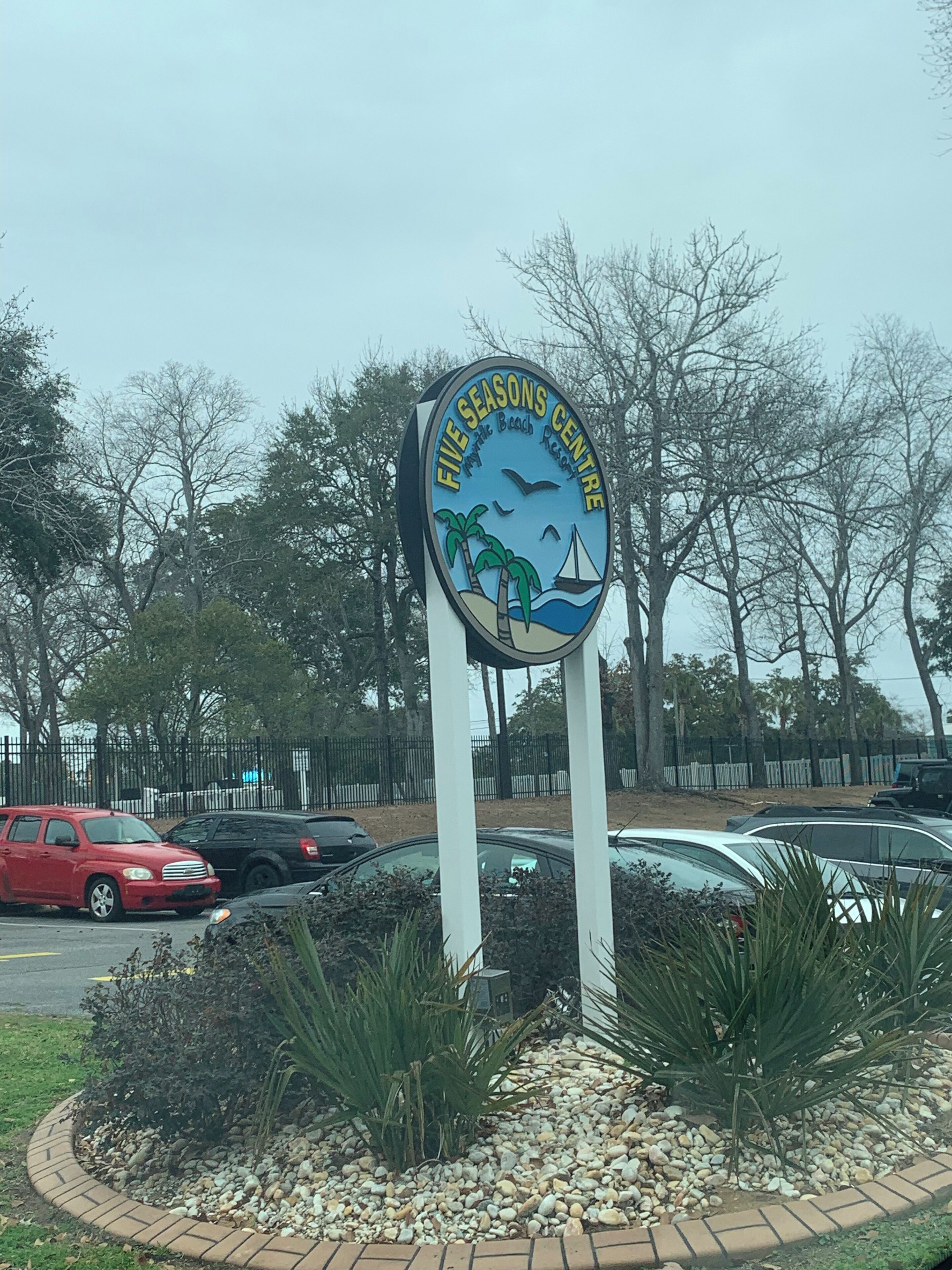 A sign for the Five Seasons Centre with a beach scene, surrounded by parked cars and trees.