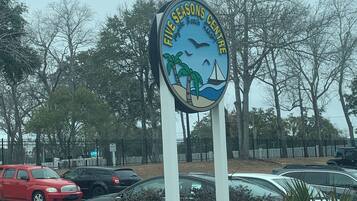 A sign for the Five Seasons Centre with a beach scene, surrounded by parked cars and trees.