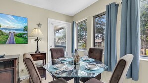 A dining room with a glass table, four chairs, a lamp, and a painting of a beach scene. - Myrtle Beach Resort 6306 (Myrtle Beach)