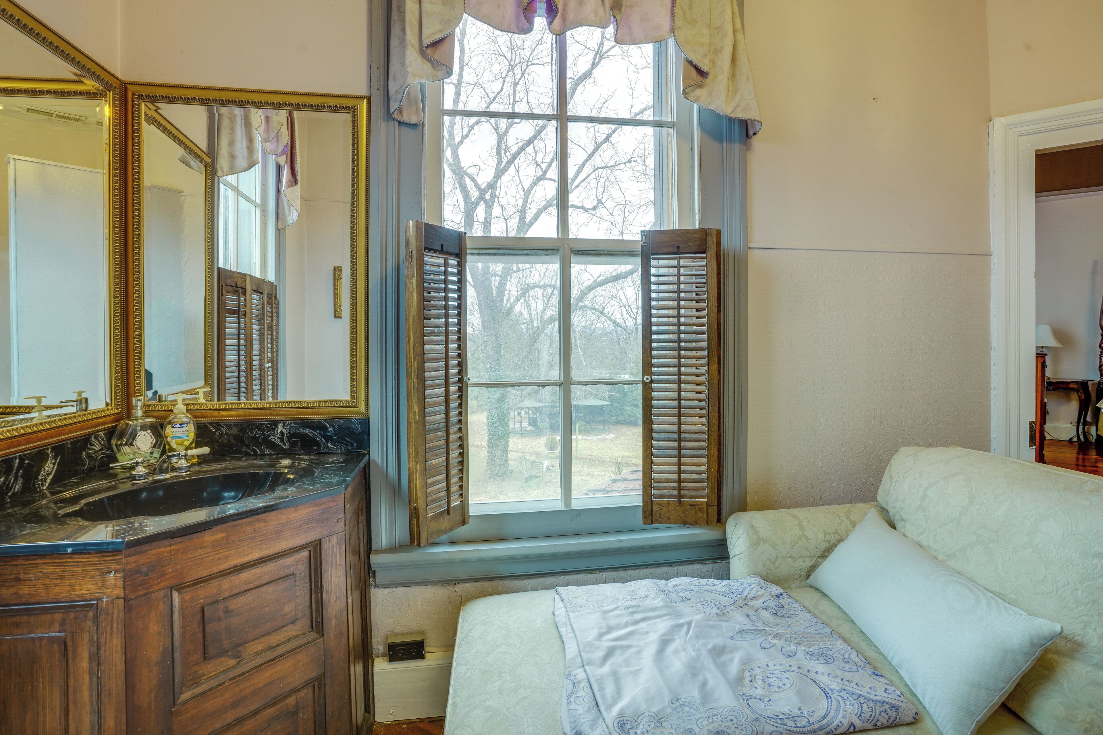 Een slaapkamer met een groot raam, een houten dressoir en een bed met kussens.