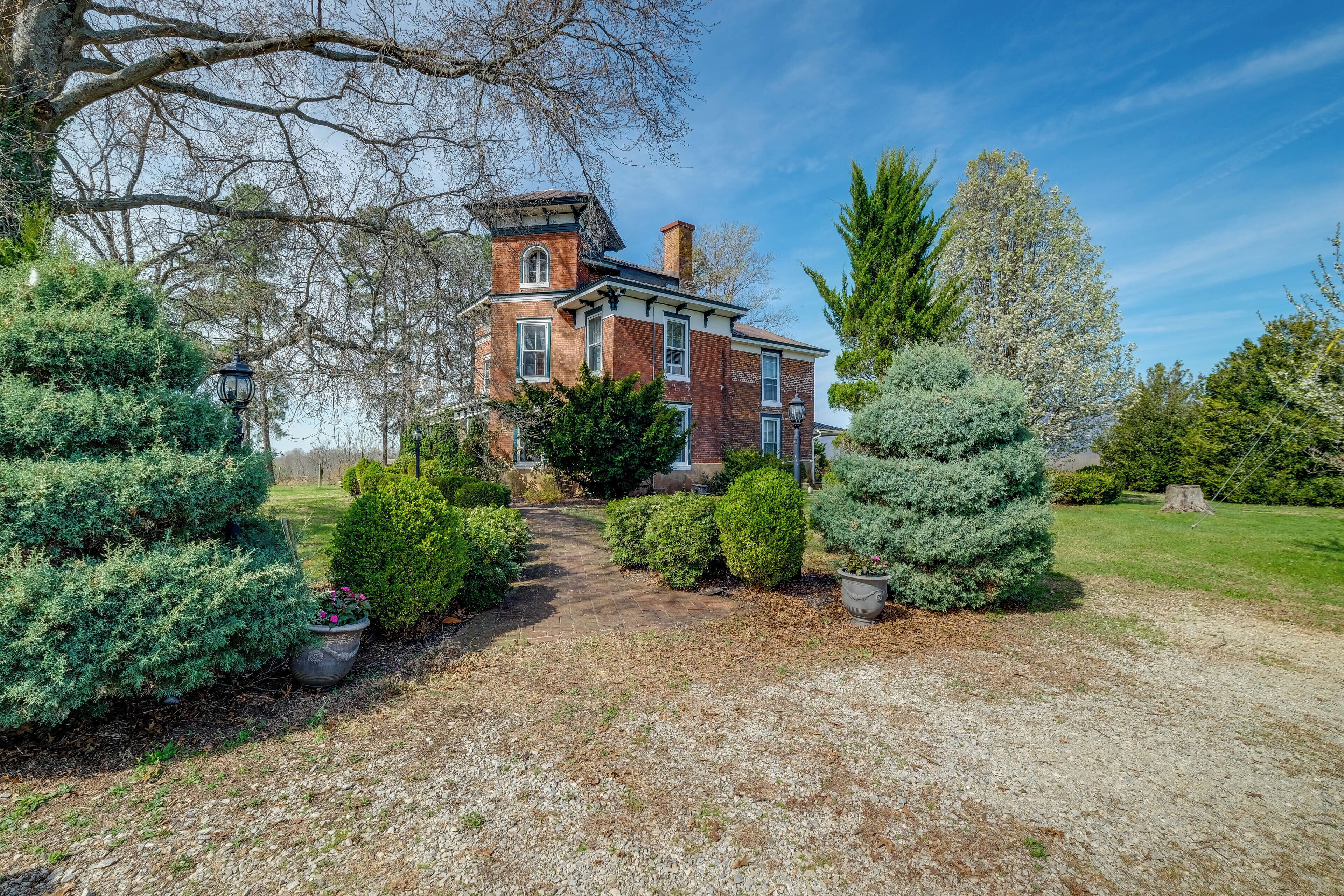 A large brick house with a tower, surrounded by well-maintained hedges and trees.