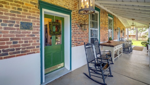 Un edificio de ladrillo con una puerta verde, un patio cubierto con mobiliario exterior y una lámpara de estilo farol.
