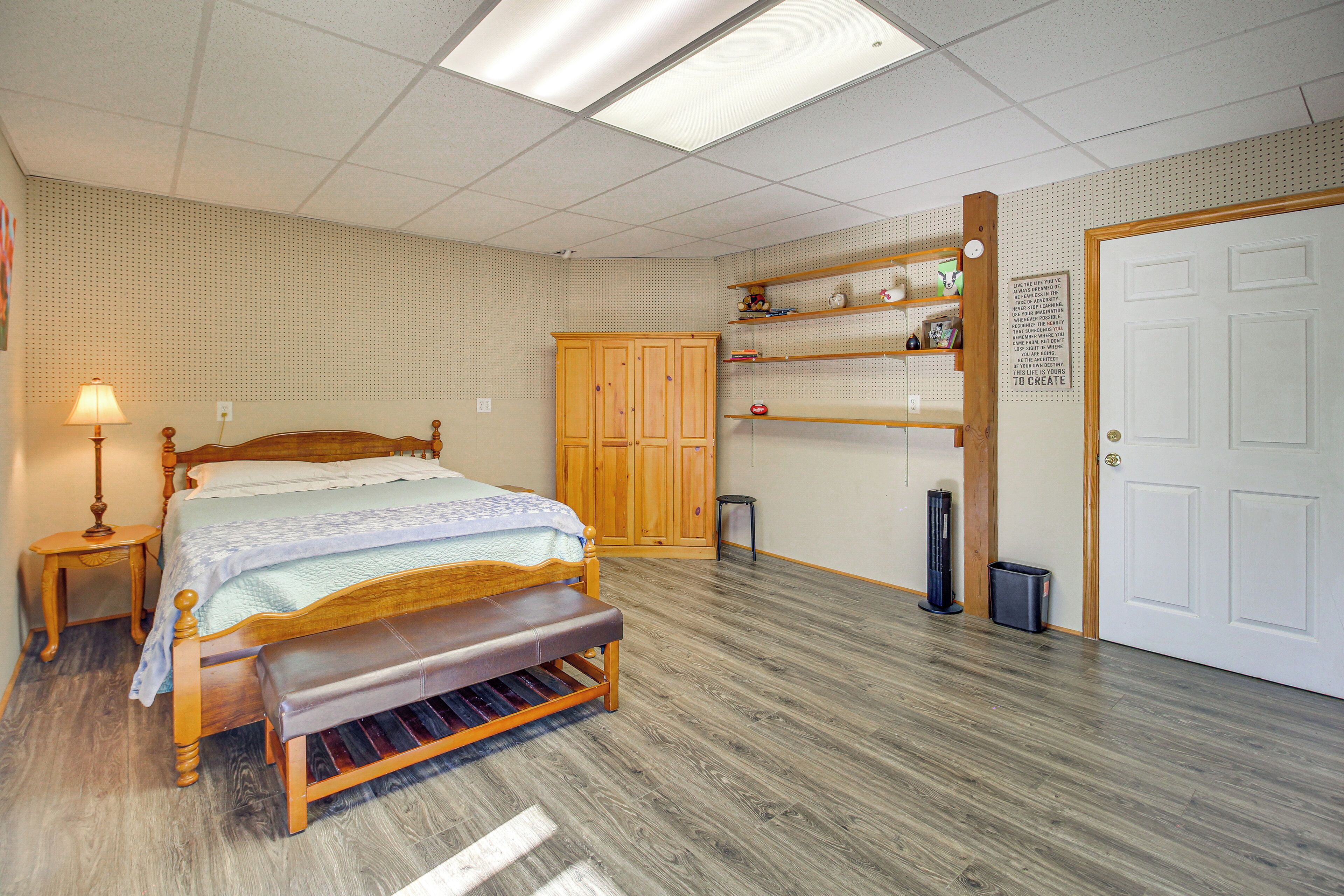 A bedroom with a wooden bed, a bench, a nightstand, a wardrobe, and a shelf with items.