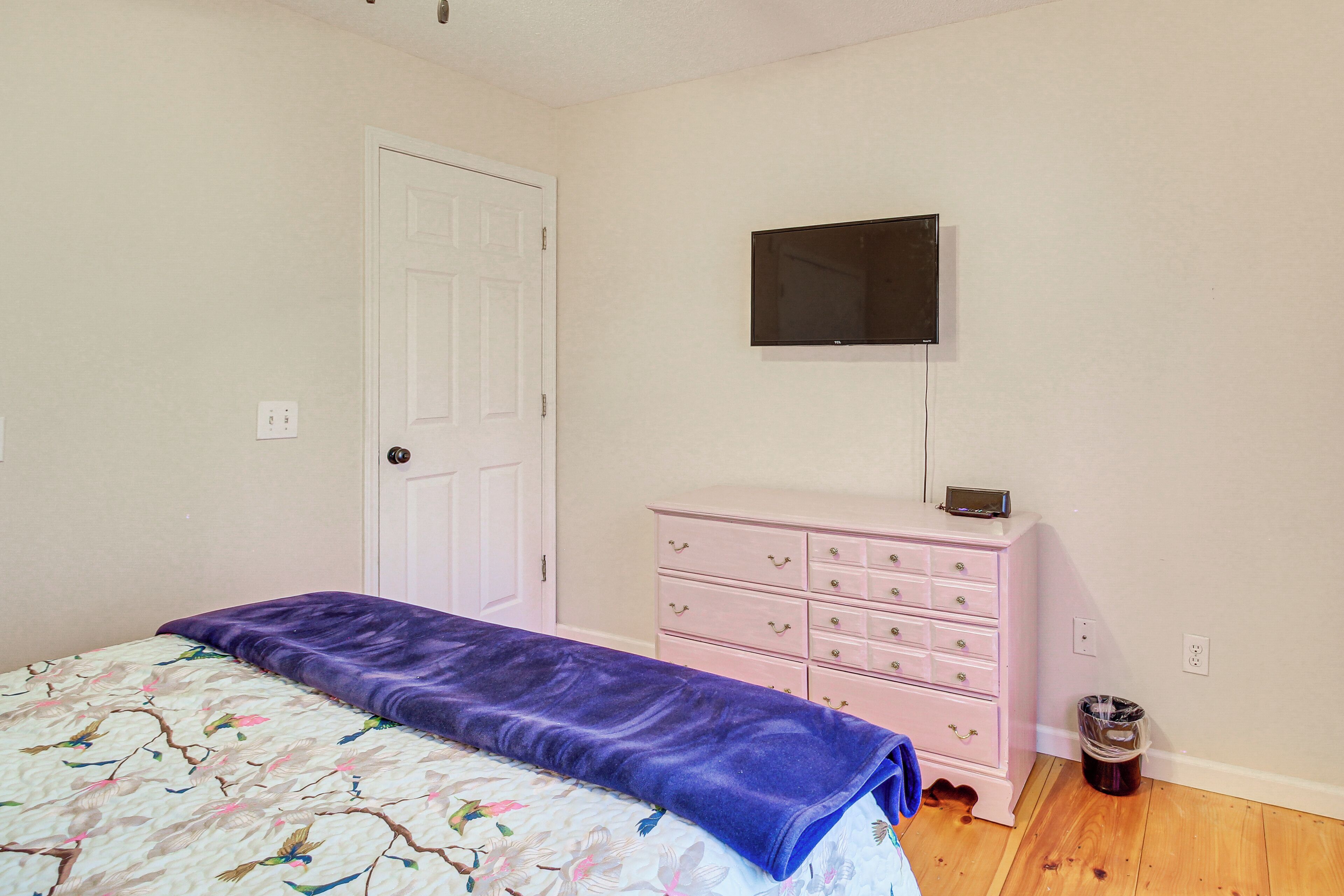 A bedroom with a bed, a dresser, a television mounted on the wall, and a door.