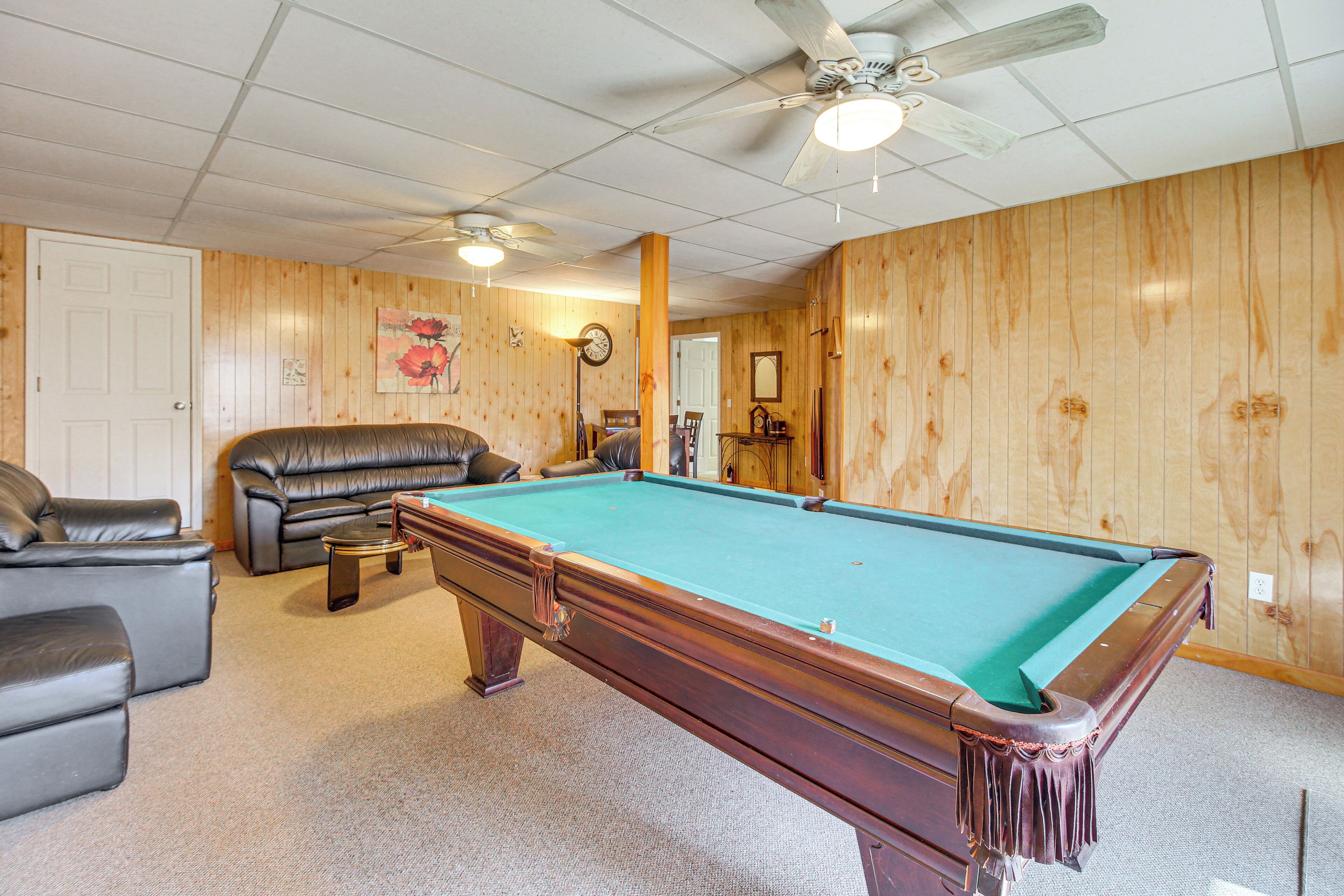A pool table in a room with wooden walls, a ceiling fan, and a leather couch.
