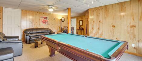 Une table de billard dans une pièce aux murs en bois, avec un ventilateur de plafond et un canapé en cuir.