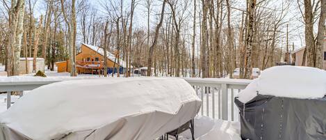 A covered outdoor grill area with a wooden deck and snow-covered surroundings.