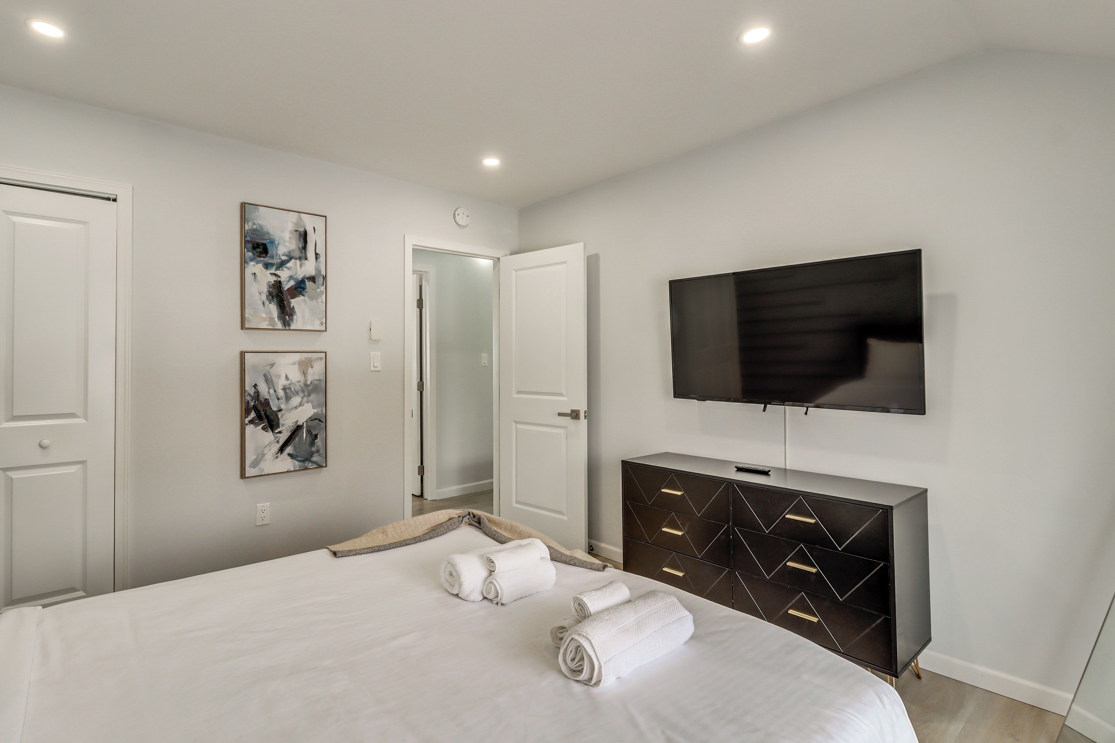 A modern bedroom with a large bed, a flat-screen TV, and a dark wooden dresser.