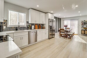 Une cuisine moderne avec des meubles blancs, un réfrigérateur en acier inoxydable et un coin repas comprenant des chaises en bois et un banc.